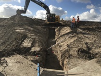 December 2019 – Two construction workers inspect a drainage channel being dug by an excavator. For more information call (619) 688-6670 or email CT.Public.Information.D11@dot.ca.gov