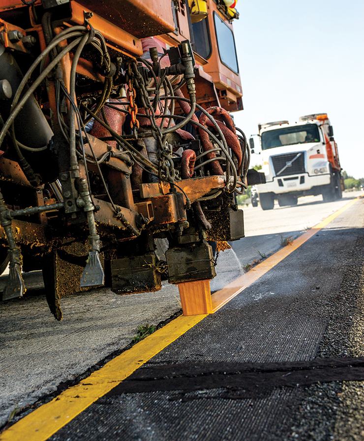 Photo shows Caltrans heavy equipment vehicle applying yellow striping to roadway