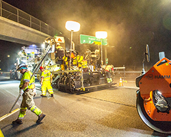 Photo of a paving machine and crew repairing pavement at night