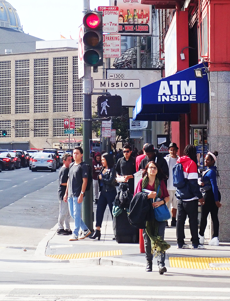 Photo of a pedestrian crossing a busy intersection in San Francisco. In the background, the pedestrian crossing light exhibiting new safety features